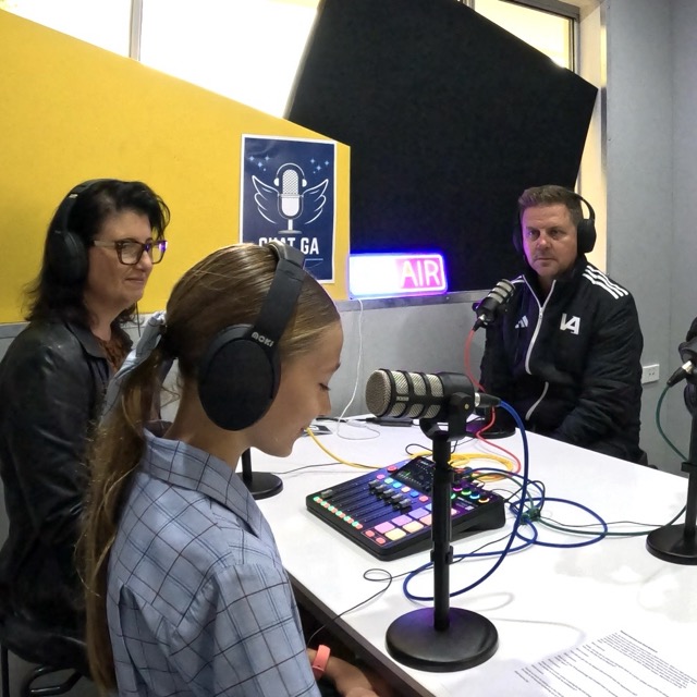 Students recording a school podcast using microphones and audio equipment in a media studio setting